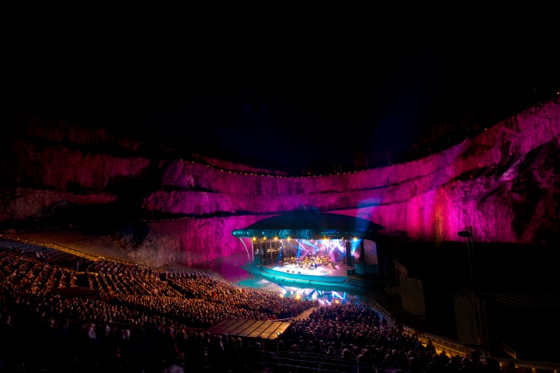 Publik njuter av en stämningsfull konsert i Dalhalla med färgsprakande ljusspel mot kalkstensväggarna.